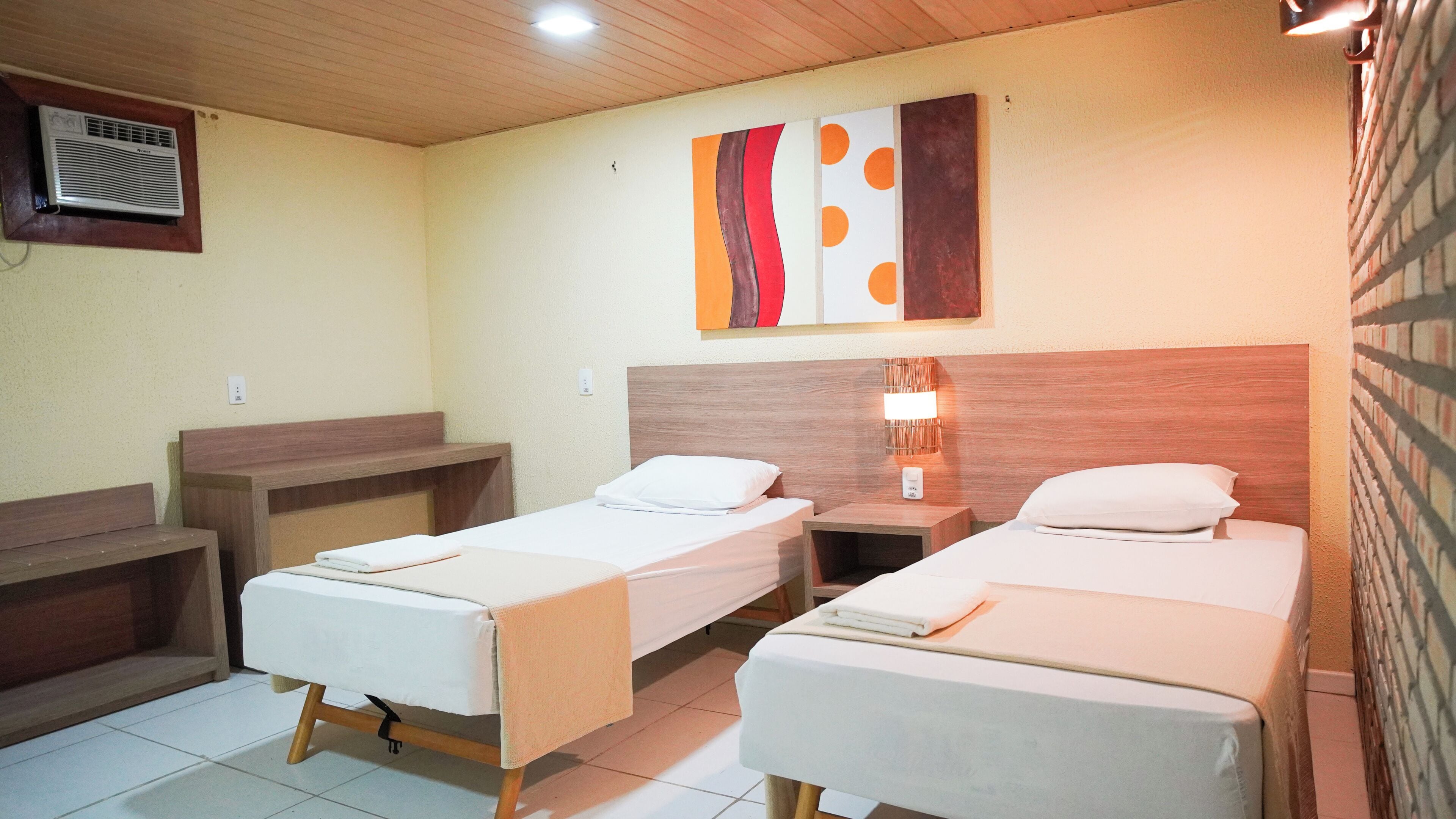 A hotel room with two single beds, a wooden headboard, a bedside lamp, and a wall-mounted air conditioner.