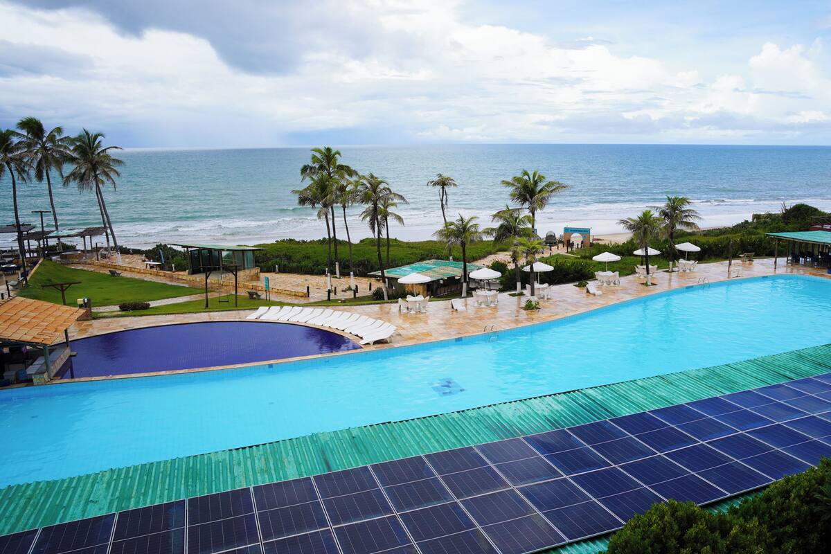 A swimming pool with a view of the ocean, surrounded by palm trees and umbrellas.
