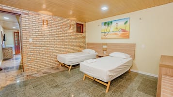 A room with two single beds, a brick wall, a wooden ceiling, and a painting of a beach scene.
