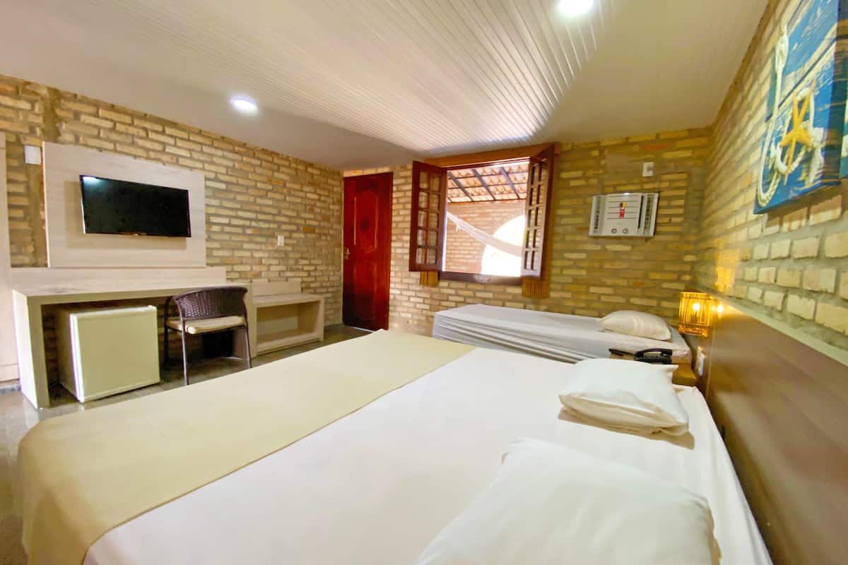 A hotel room with a bed, a desk, a TV, a window with a view, and a wall-mounted heater.
