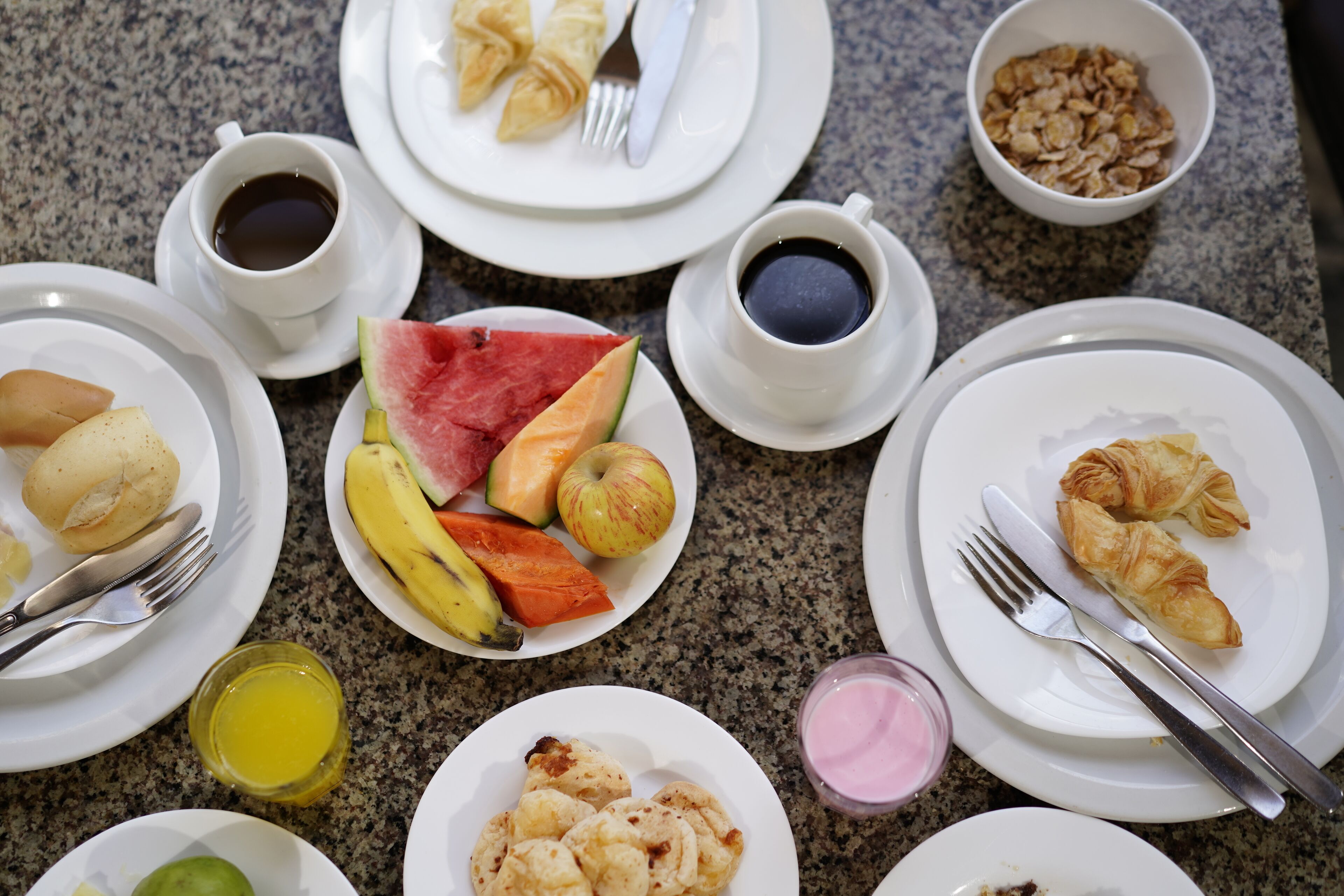 Colazione servita con piatti di cibo, tra cui croissant, frutta e bevande.