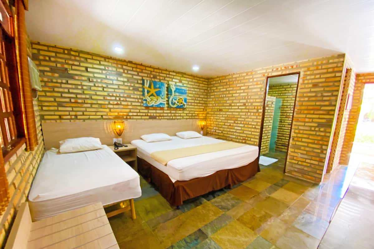 A room with a brick wall, a bed with a headboard, a bedside table with a lamp, and a door.