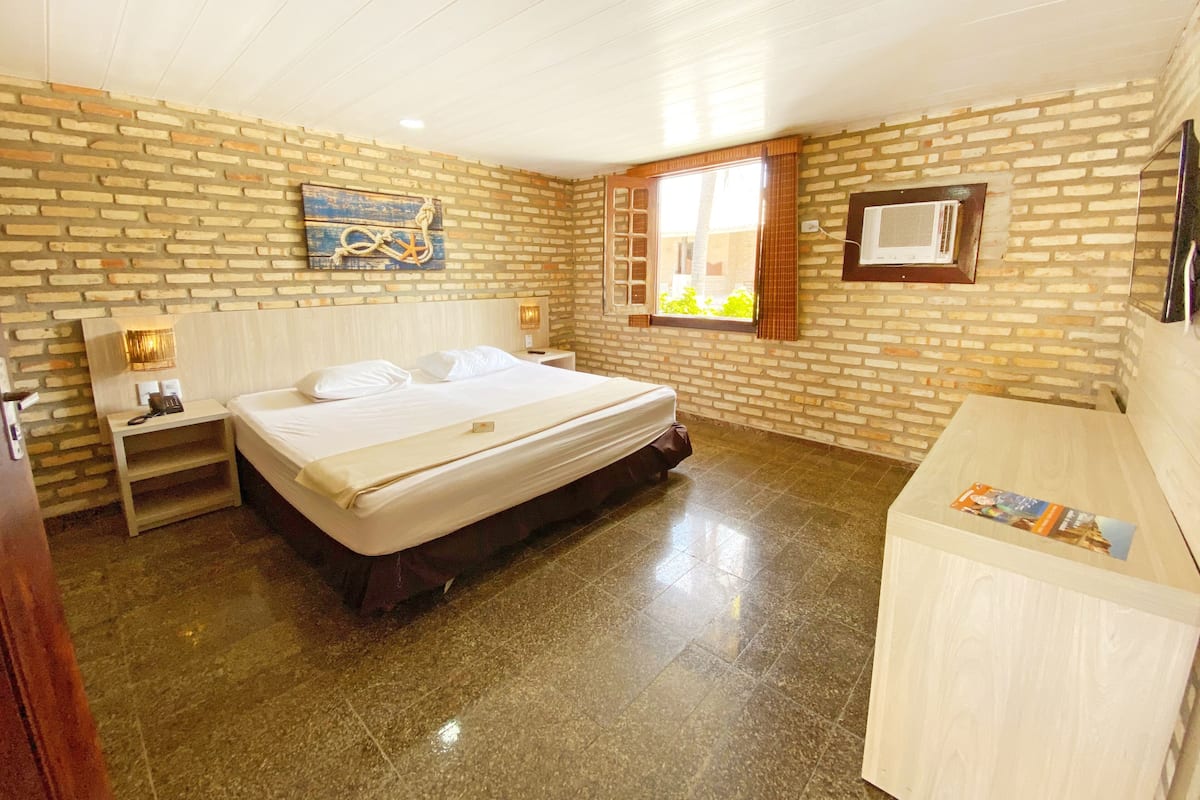 A hotel room with a brick wall, a bed, a nightstand, a desk, and a window with a view.