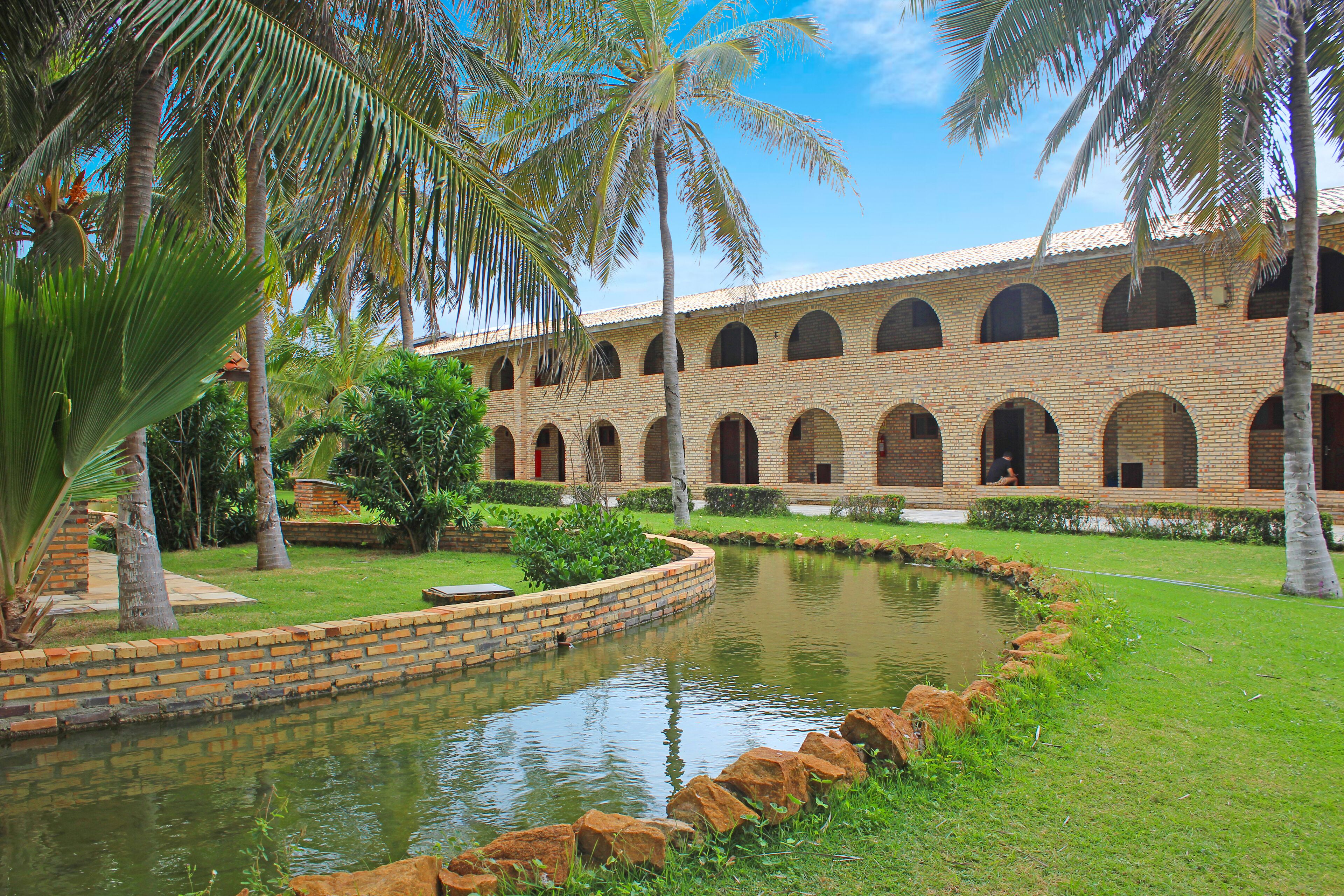 A courtyard with a brick building, a pond, and palm trees.