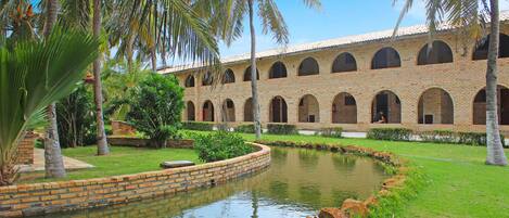 A courtyard with a brick building, a pond, and palm trees.