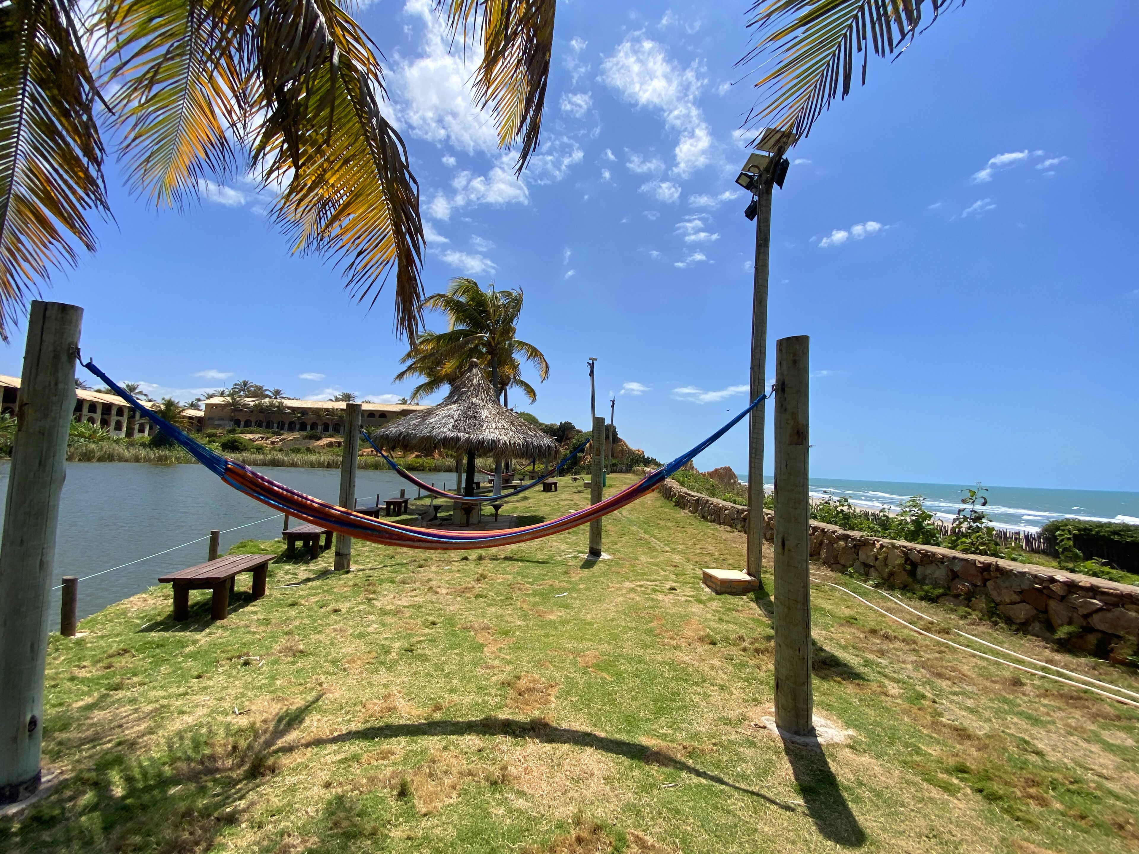 A hammock strung between wooden posts, a thatched-roof gazebo, and a view of the ocean.