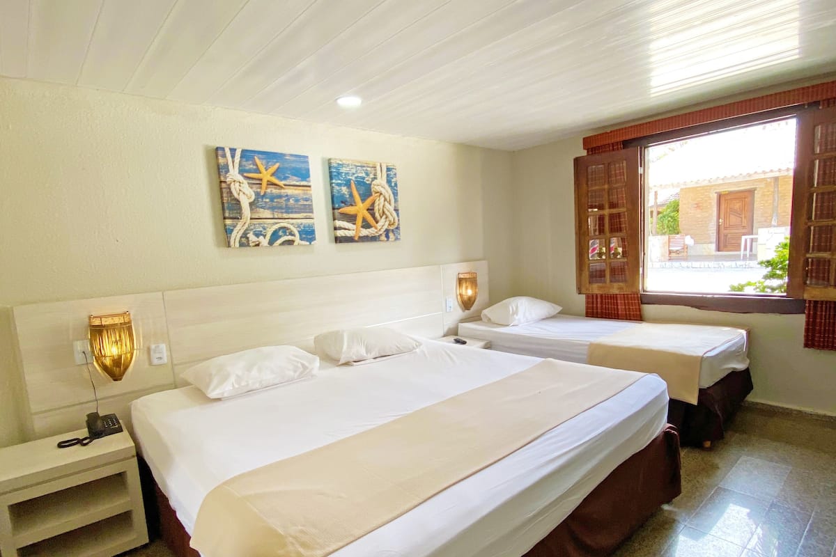 A hotel room with two beds, a nightstand, a wall-mounted lamp, and artwork depicting nautical themes.