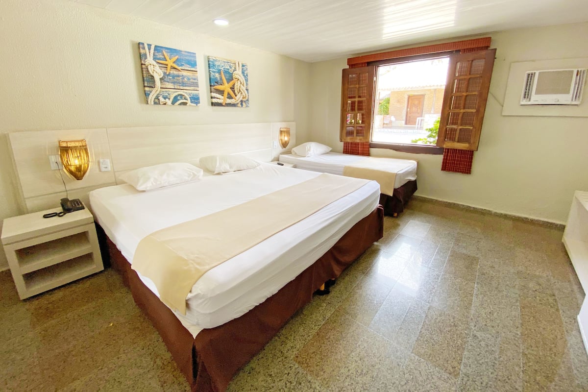 A hotel room with a large bed, two bedside tables, a nightstand, a window with curtains, and wall-mounted artwork.