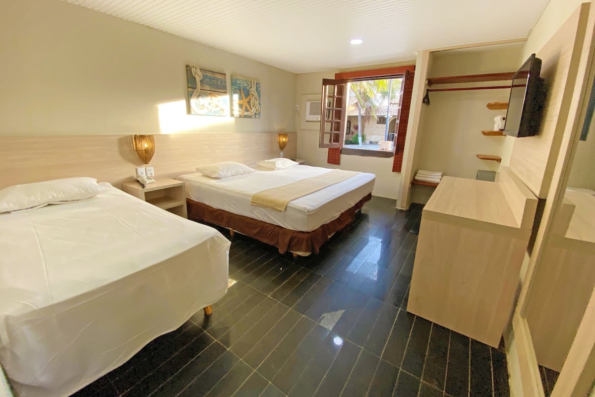 A hotel room with two beds, a small desk, a window with a view, and a bathroom area.