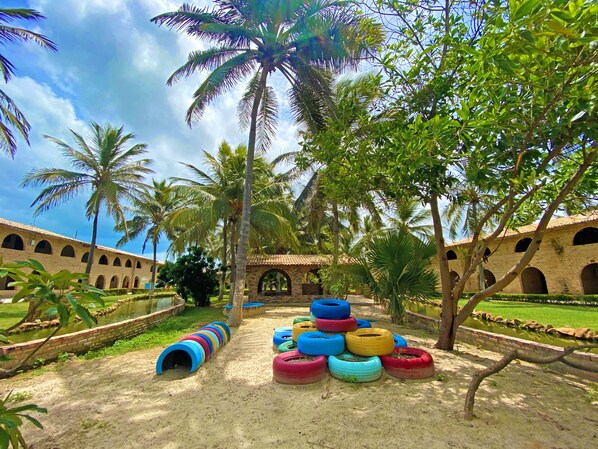 Un patio con palmeras, un edificio de ladrillo con arcos y neumáticos de colores dispuestos en círculo.