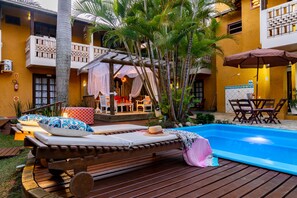 A poolside area with wooden loungers, a covered seating area, and a pool.
