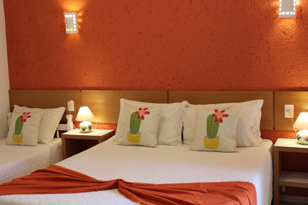 A hotel room with two beds, each with a cactus pillow, a wooden headboard, and a nightstand with a lamp.