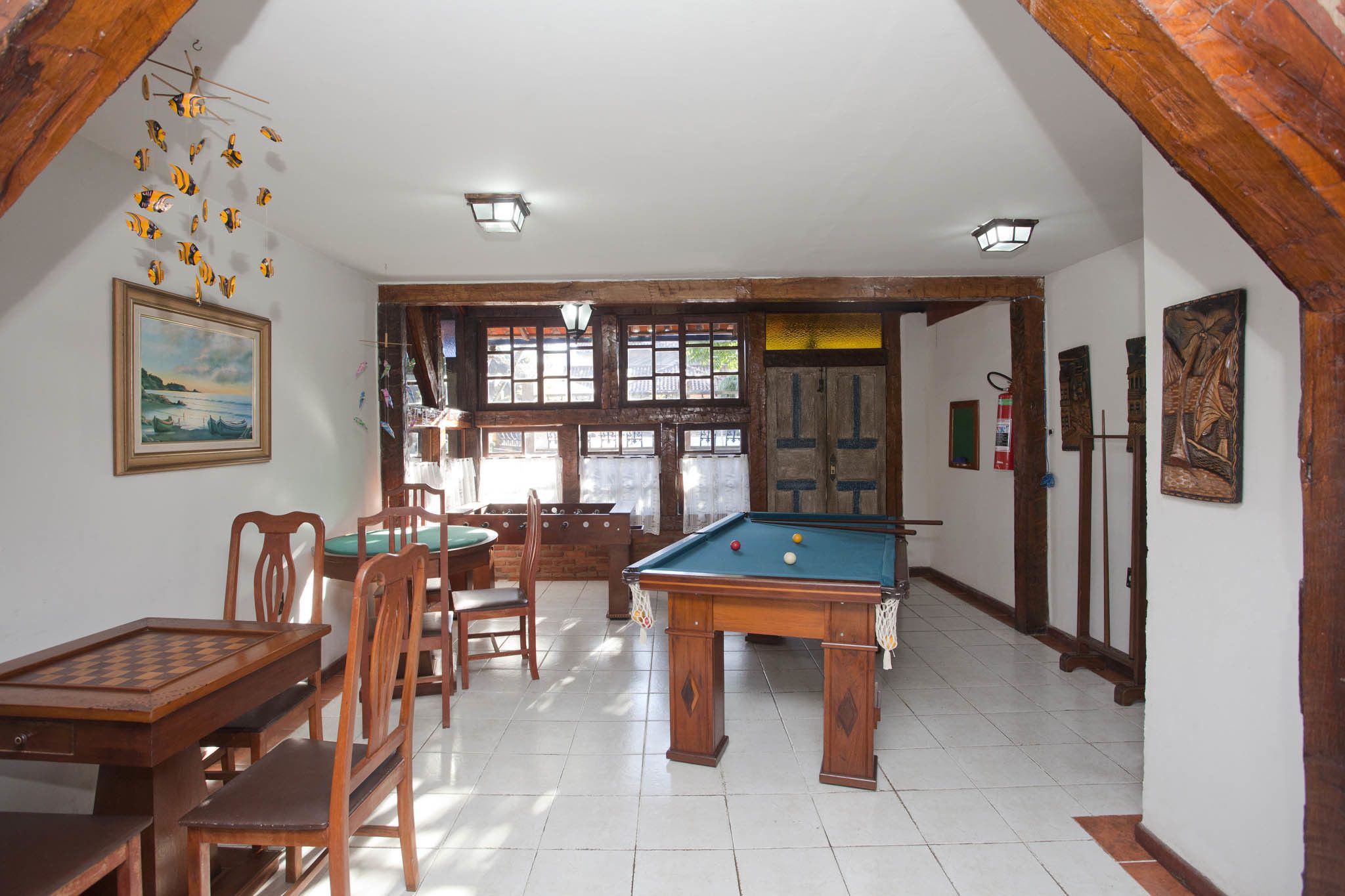 Quarto com mesa de bilhar, cadeiras de madeira, mesa de jantar e um quadro na parede.
