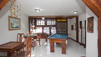 Quarto com mesa de bilhar, cadeiras de madeira, mesa de jantar e um quadro na parede.