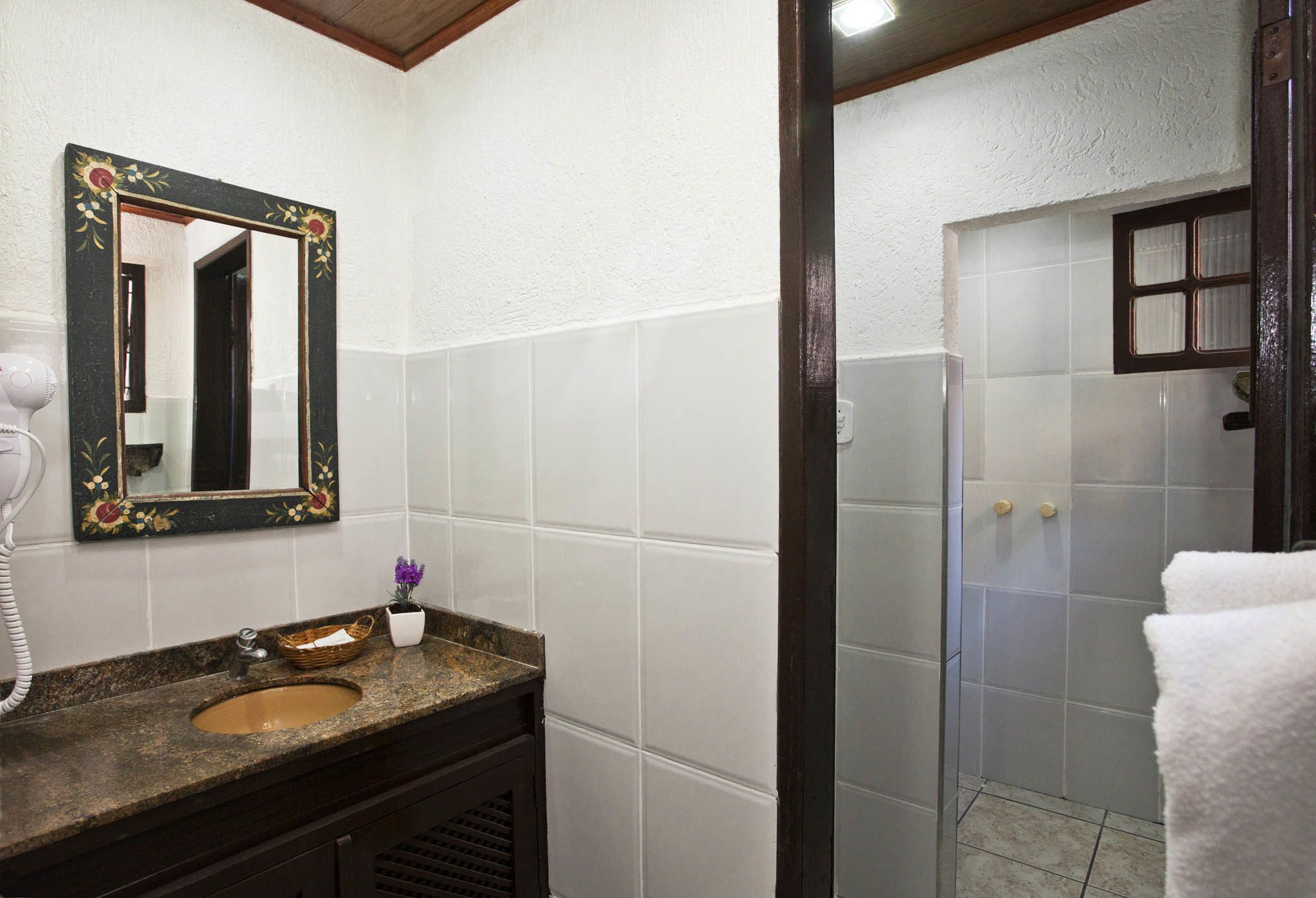 Une salle de bain dotée d’un comptoir en granit, d’un lavabo, d’un miroir avec un cadre floral, d’un sèche-cheveux et d’un espace douche avec une porte en verre.