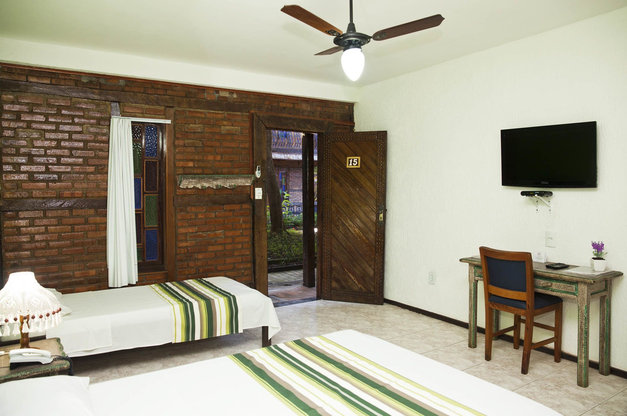 A room with two beds, a desk with a chair, a television, and a ceiling fan.