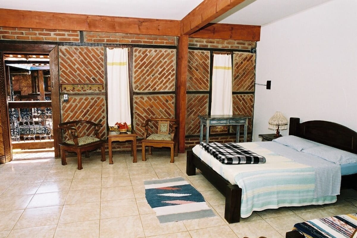 A bedroom with a bed, two chairs, a small table, a lamp, and a patterned rug.