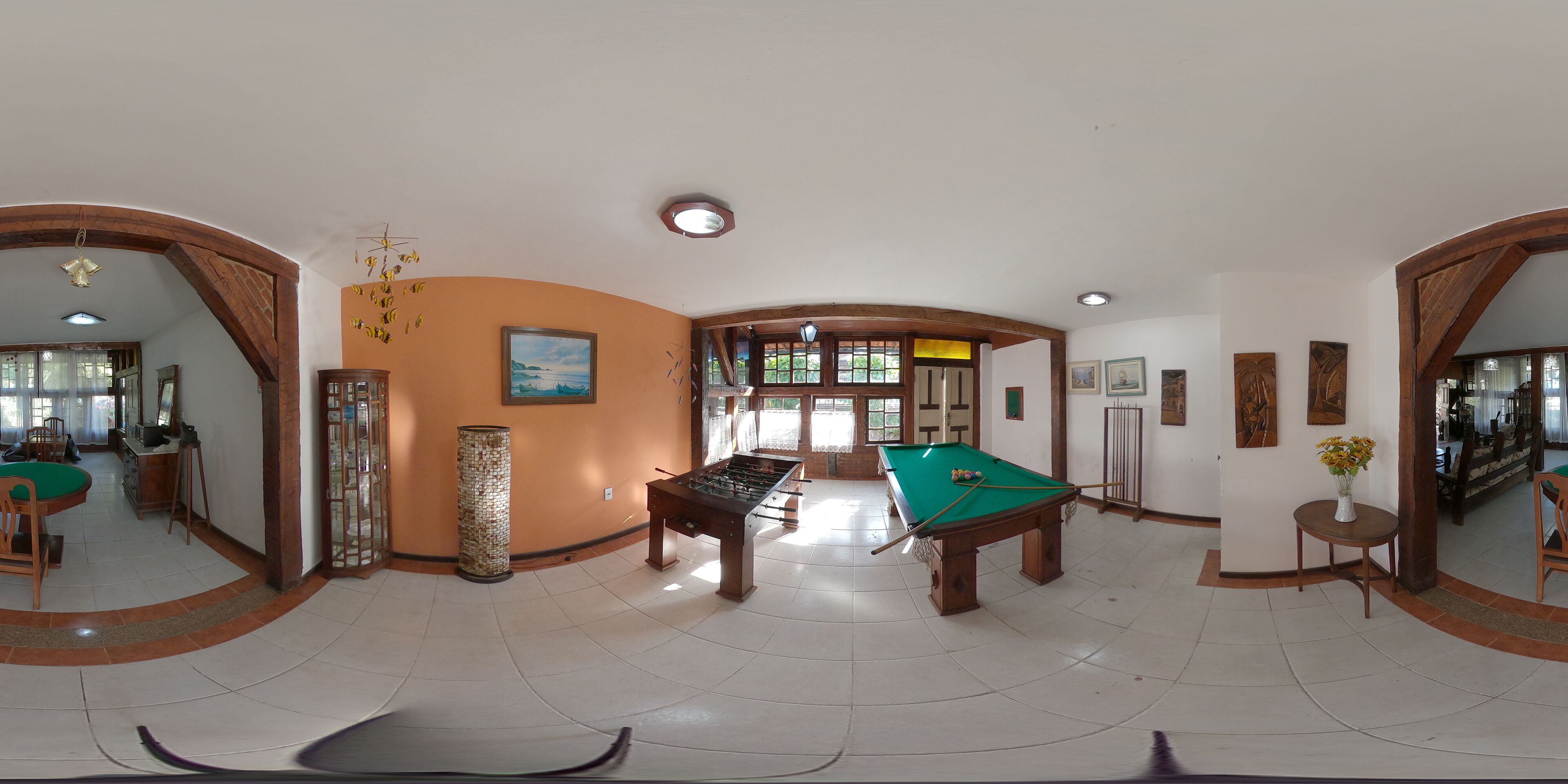 A spacious indoor area with a pool table, a foosball table, and a billiards table. There are wooden arches framing the space, and a large mirror on one wall.