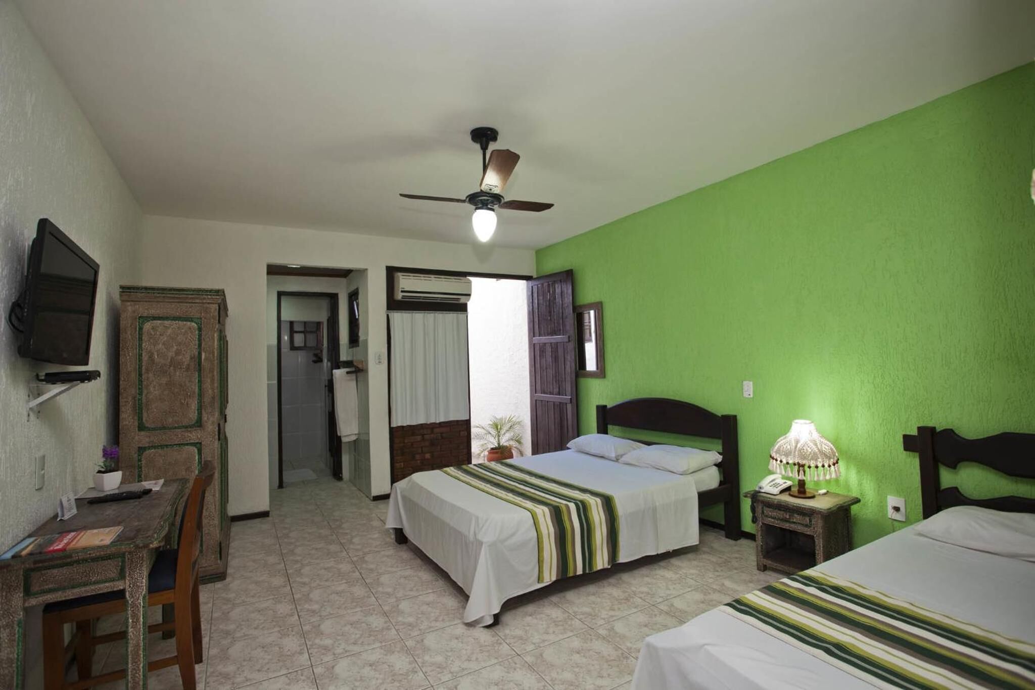A room with a bed, a desk with a chair, a television, and a ceiling fan.
