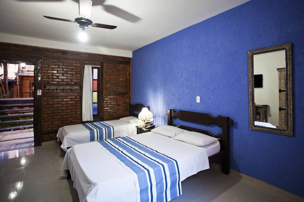 A room with two beds, a ceiling fan, a mirror, and a brick wall.