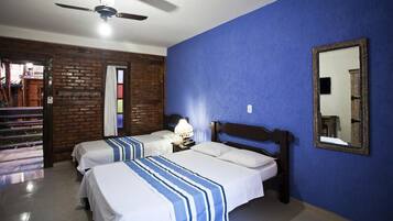 Habitación de hotel con dos camas, ventilador de techo, espejo y pared de ladrillo.