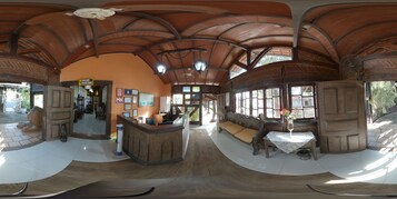 Un vestíbulo espacioso con un mostrador de recepción de madera, una zona de estar con un banco y un espejo grande que refleja el interior.