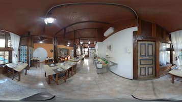 Un comedor amplio con varias mesas y sillas, un espacio tipo bufé y una cocina visible al fondo.