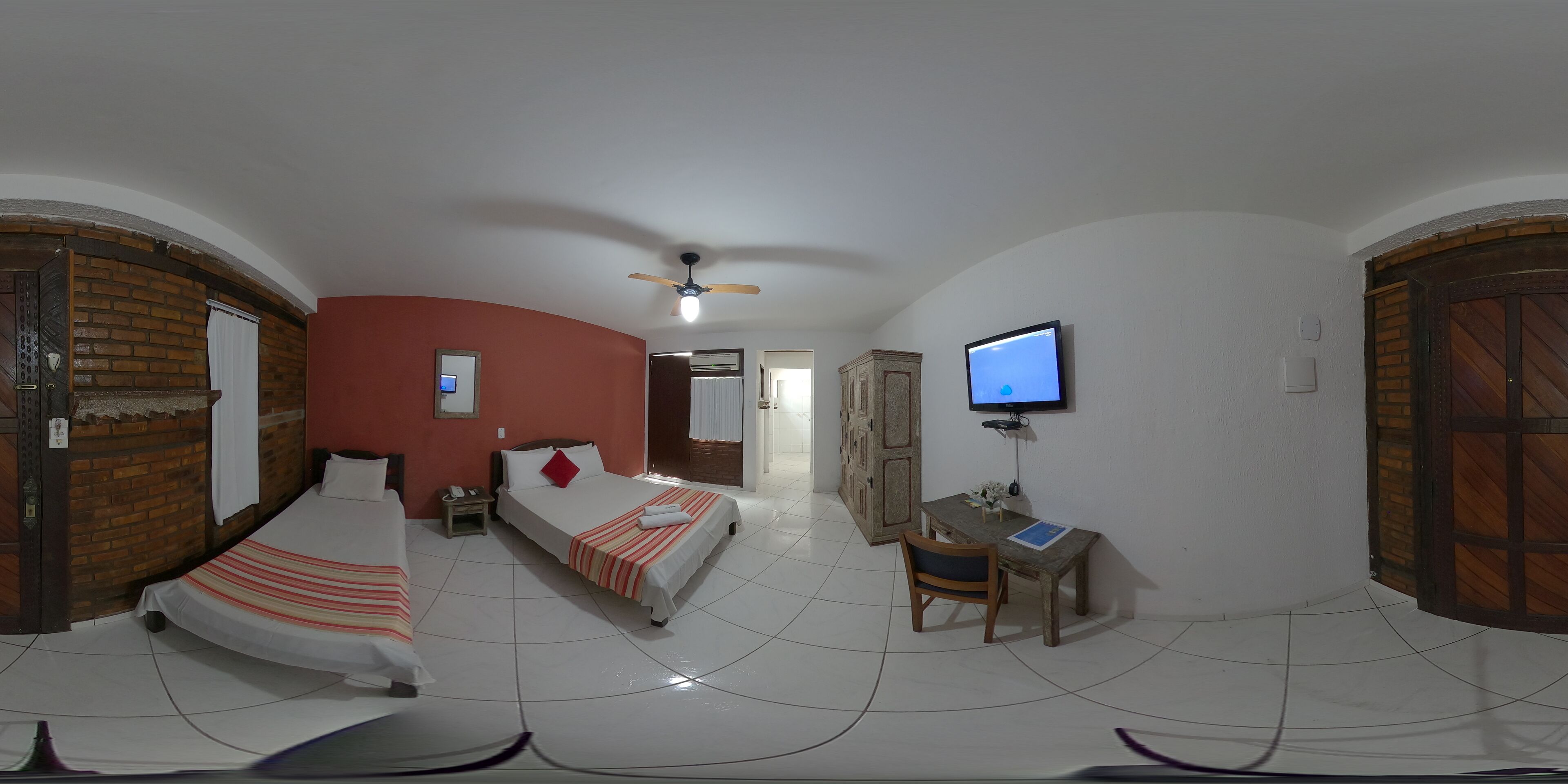 Una habitación con dos camas, un escritorio, un televisor y un ventilador de techo.
