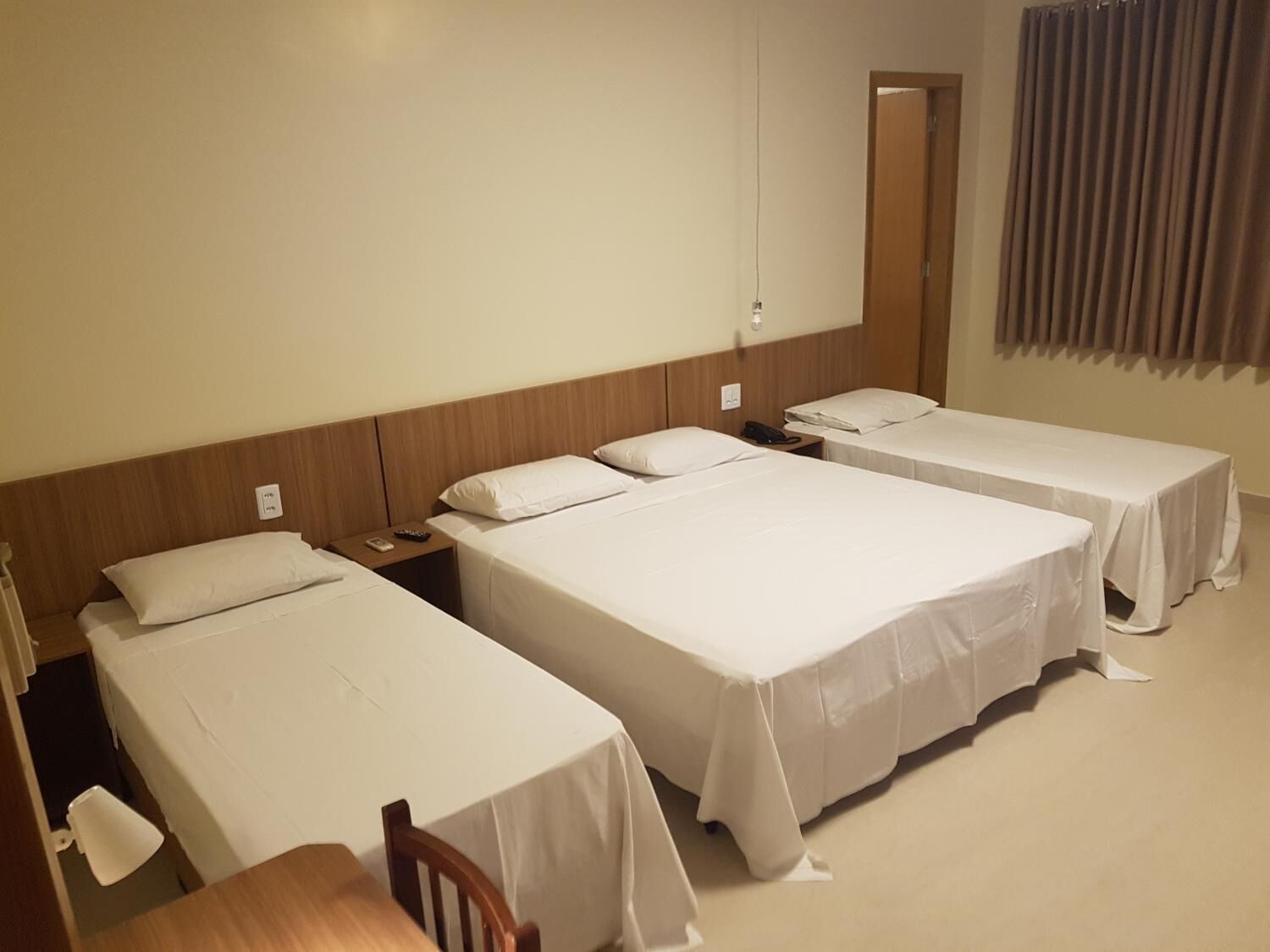 A hotel room with three single beds, a wooden headboard, a small table, and a chair.