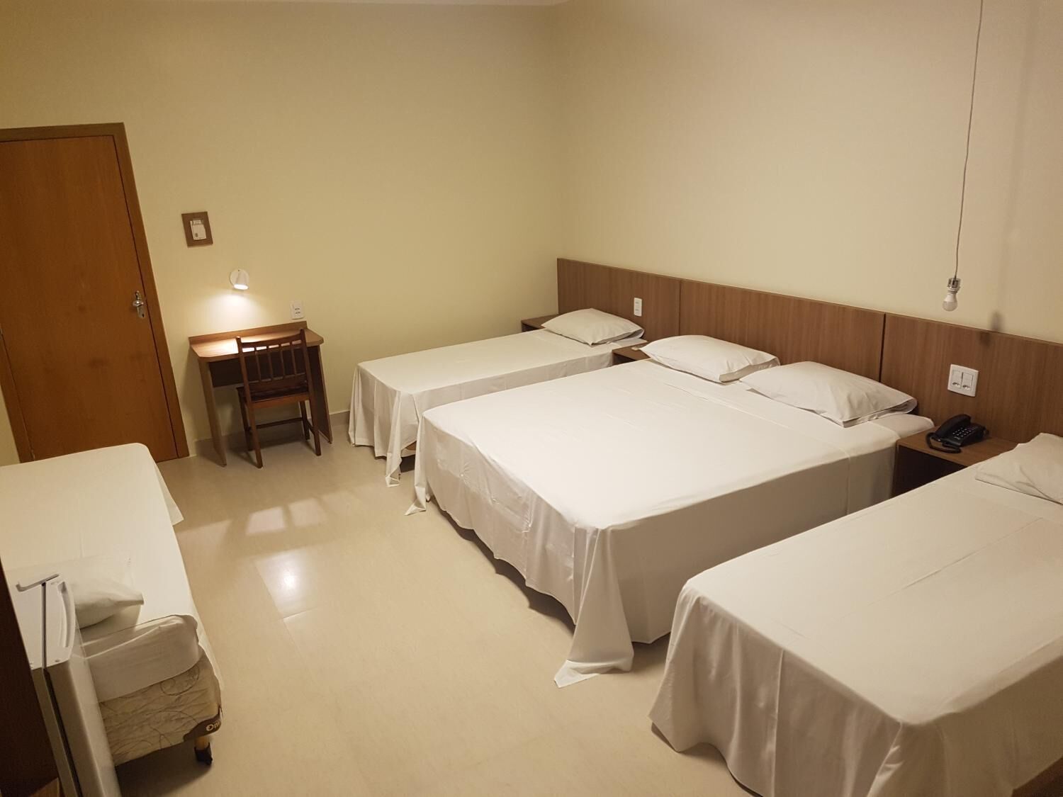 A hotel room with three single beds, a desk, and a chair.