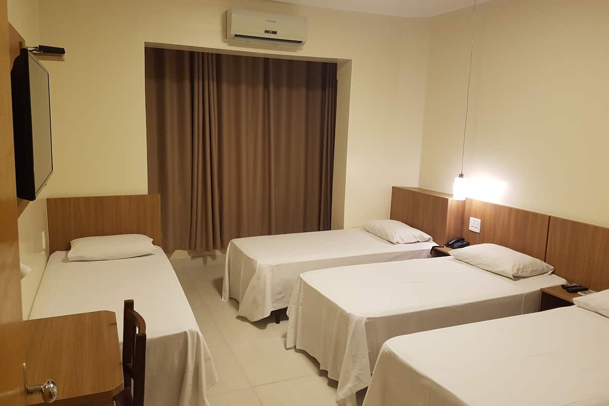 Une chambre d’hôtel avec trois lits simples, une tête de lit en bois, un téléviseur à écran plat, un bureau et un appareil de climatisation.