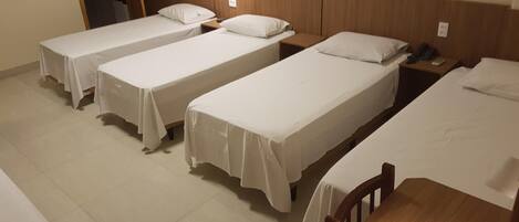 Una habitación de hotel con cuatro camas individuales alineadas, una mesita de noche de madera con un teléfono y una mesa de madera.