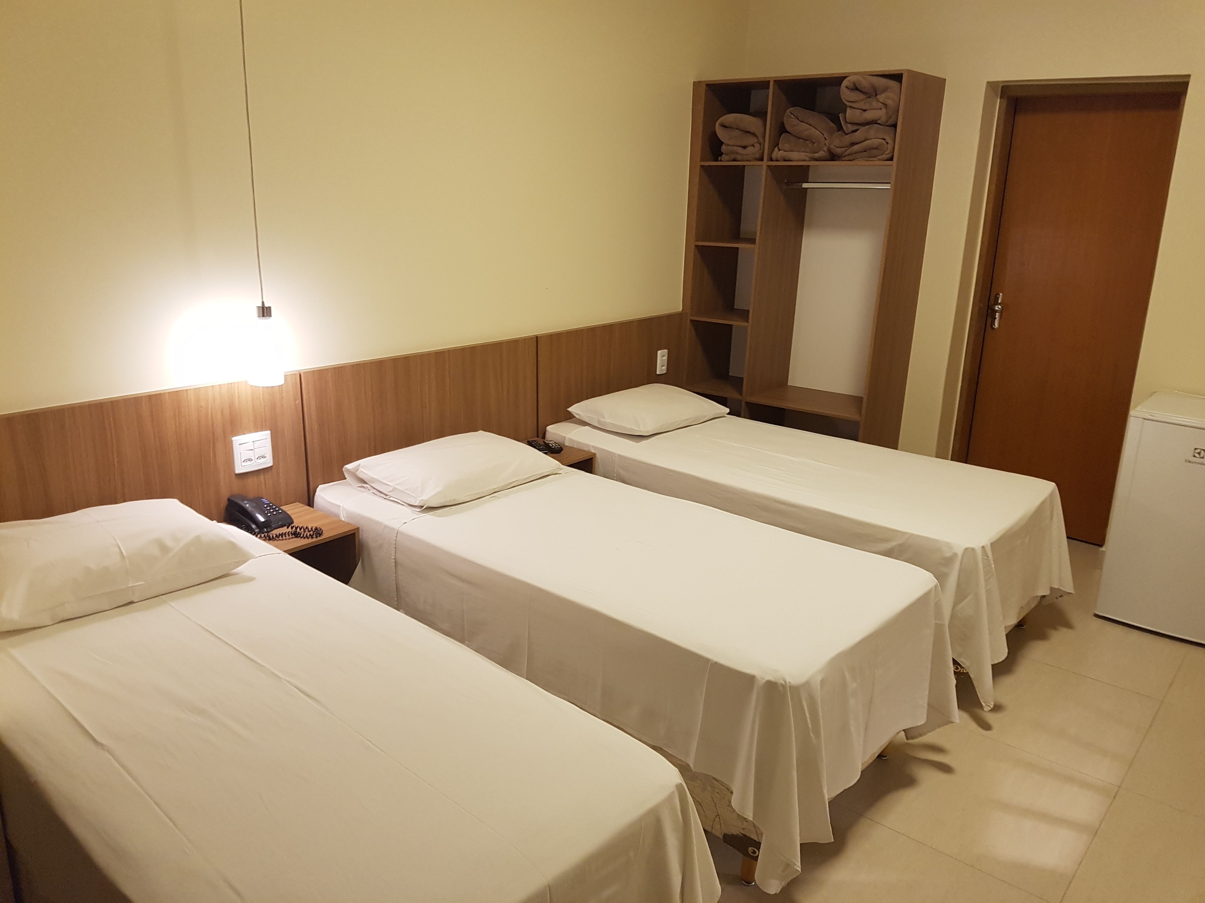 Ein Hotelzimmer mit zwei Einzelbetten, einem Kleiderschrank, einem Schreibtisch mit Telefon und einem kleinen Kühlschrank.