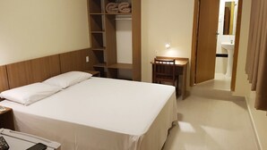 Een hotelkamer met een bed, een houten garderobe, een bureau met een lamp en een badkamer die door een open deur zichtbaar is.