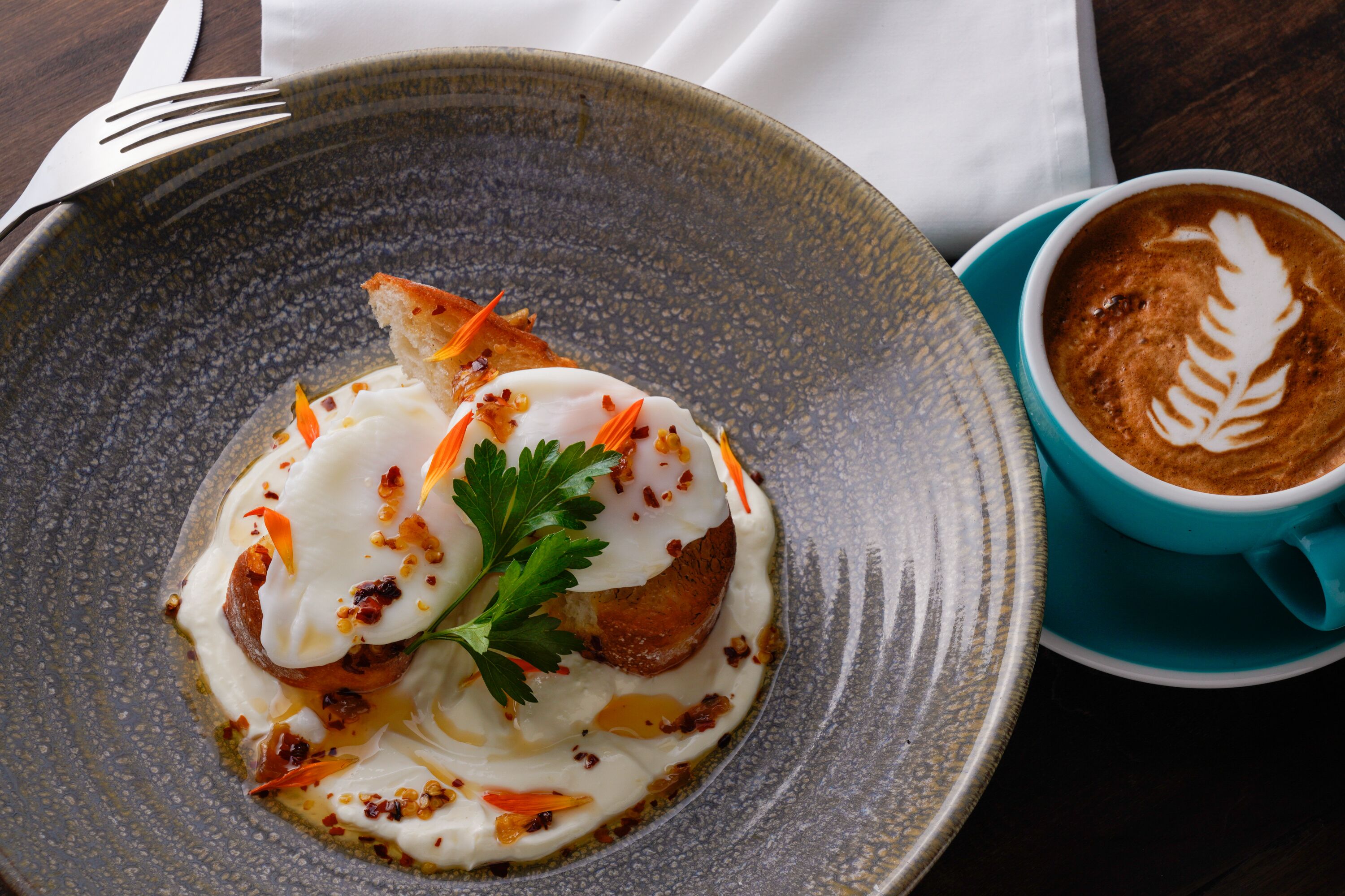 Un plato de comida con decoración, una taza de café con arte de latte, y una servilleta sobre una mesa.