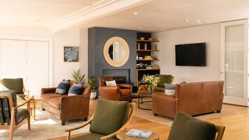 A modern living room with leather sofas, wooden chairs, a fireplace, a television, and a bookshelf.