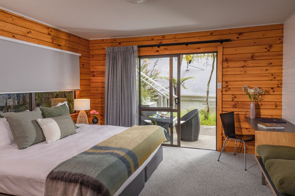 A modern hotel room with a large bed, a desk, and a balcony with outdoor seating.
