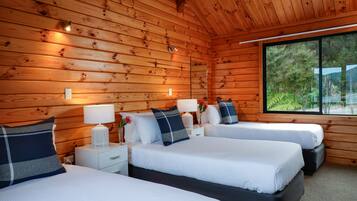 Una cabaña con tres camas, paredes de madera y un ventanal con vistas a árboles.