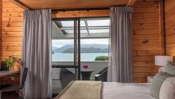 Una habitación de cabaña de madera con una cama, un escritorio y vistas a un lago y montañas a través de un ventanal.