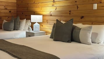 A room with two beds, wooden walls, a nightstand with a lamp, and several pillows.