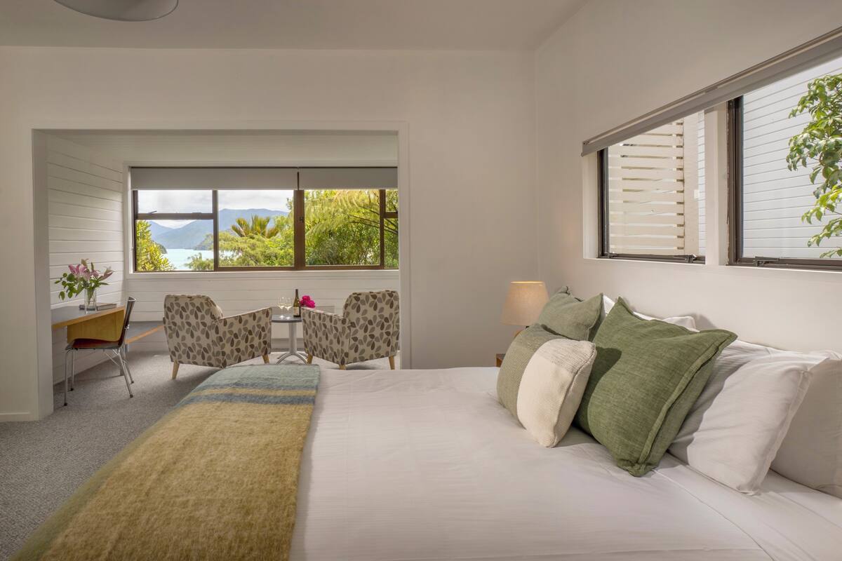 A bedroom with a bed, a desk, a chair, and a view of the outdoors.