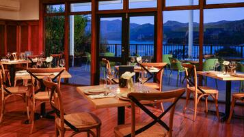 Un restaurante con mobiliario de madera y amplias ventanas que ofrecen vistas a montañas y un lago.