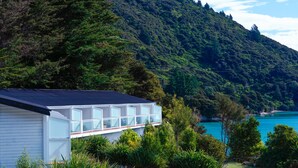 A modern house with large windows, surrounded by lush greenery and a view of a lake. - The Portage Resort (Portage)