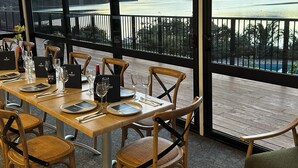 A dining area with a view of a lake and mountains, featuring wooden tables and chairs, wine glasses, and menus. - The Portage Resort (Portage)
