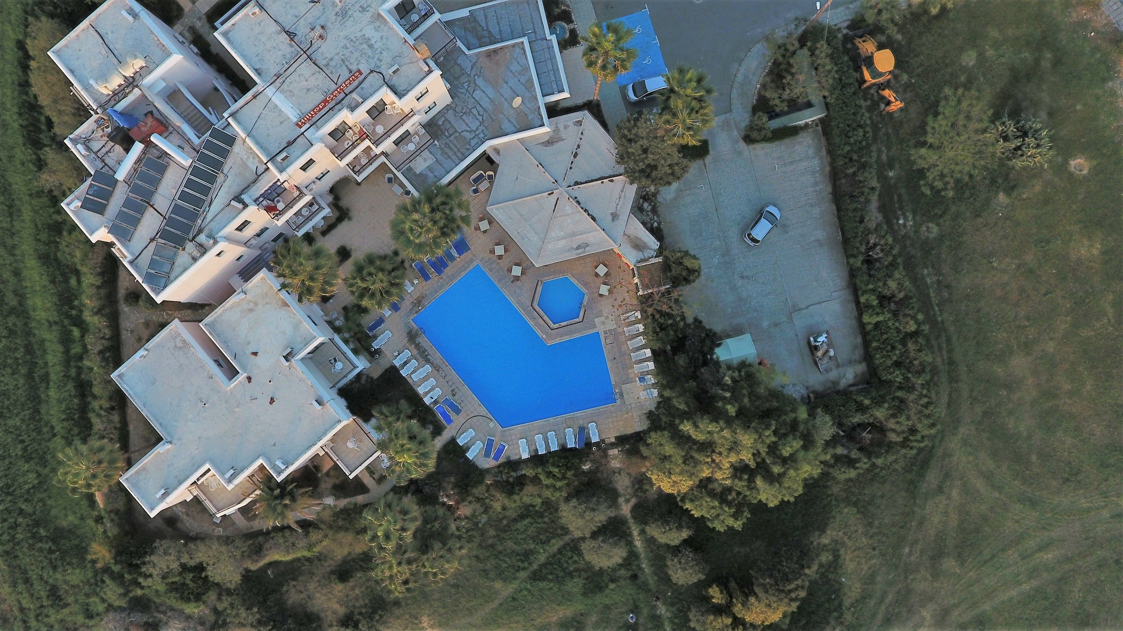 Vue aérienne d’un complexe résidentiel comprenant plusieurs bâtiments, une piscine et un espace de stationnement.