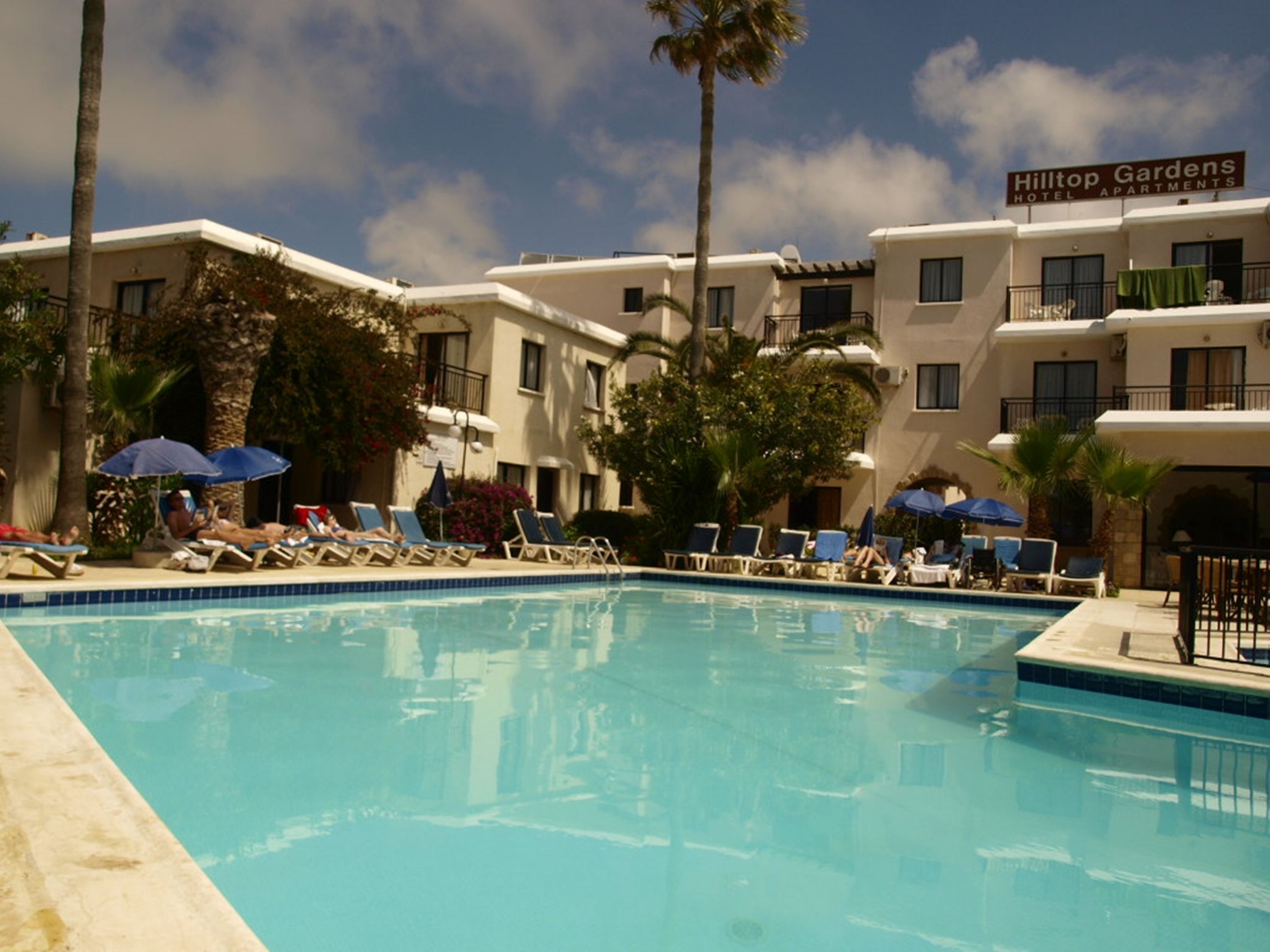 A hotel pool area with lounge chairs and umbrellas, surrounded by buildings with balconies.