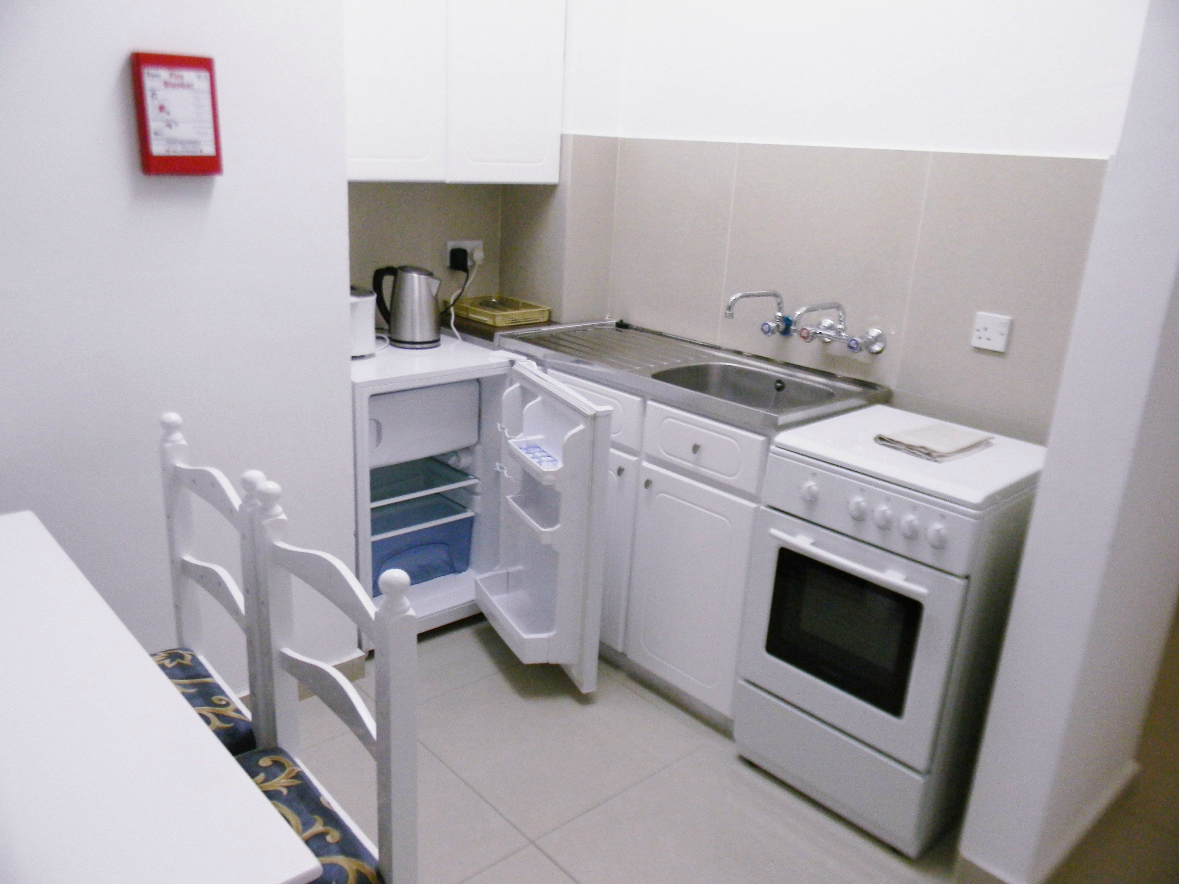Une cuisine compacte avec des meubles blancs, un four encastré, un évier et une machine à café.