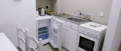 Une cuisine compacte avec des meubles blancs, un four encastré, un évier et une machine à café.