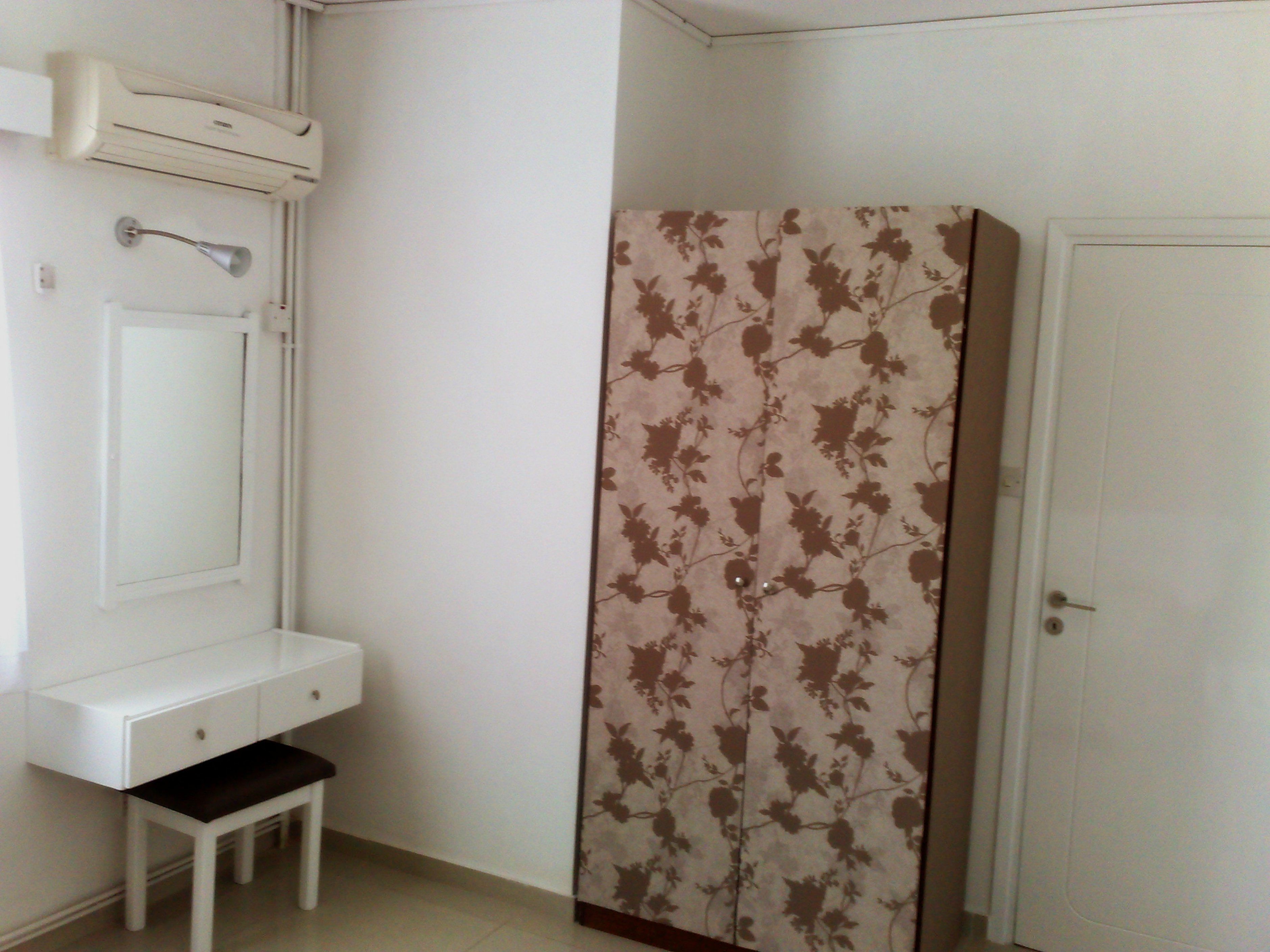 A room with a white vanity, a small bench, a door, and a wardrobe with floral wallpaper.