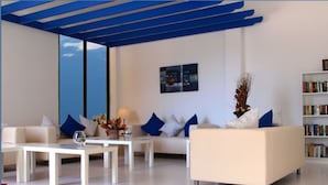 Uma sala de estar moderna com um sofá branco, almofadas azuis, uma mesa de centro e uma estante.